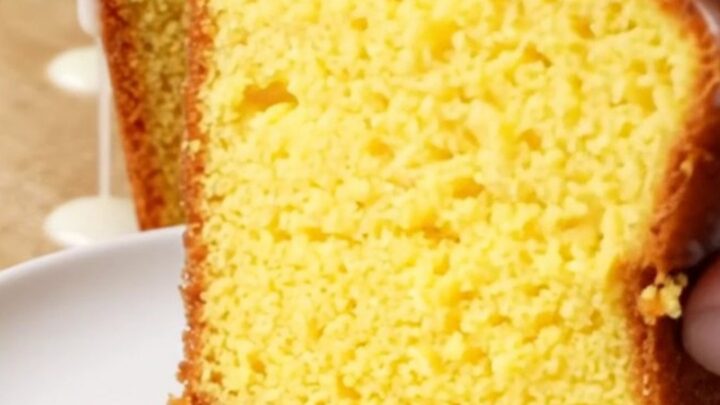 Golden whole lemon loaf cake with white glaze on a cutting board, slice cut showing moist yellow crumb.