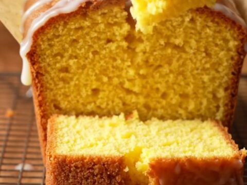 A golden whole lemon blender pound cake with white glaze on a cutting board, one slice cut showing moist crumb.