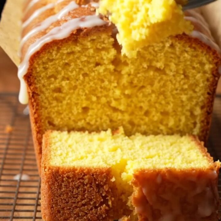 A golden whole lemon blender pound cake with white glaze on a cutting board, one slice cut showing moist crumb.