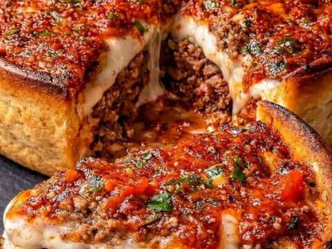 A golden, crispy deep-dish meatball parmesan pie on a black slate, with a slice removed to show the layers.