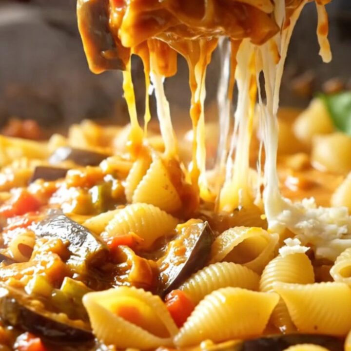 A skillet of roasted eggplant and tomato shell pasta with melted mozzarella and fresh basil