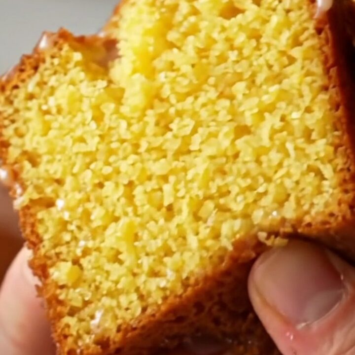 Whole lemon blender pound cake with white glaze on a wooden board.