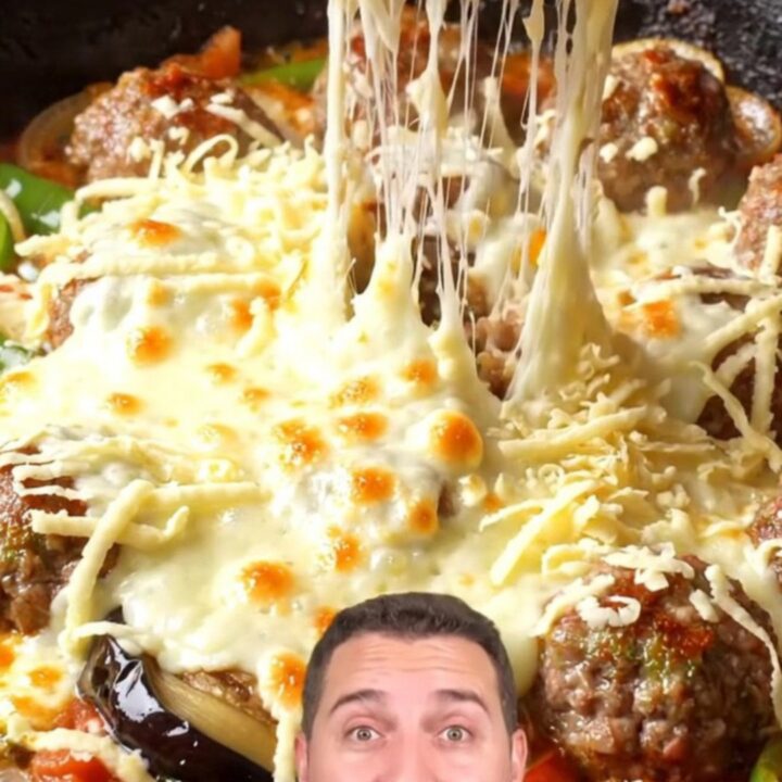 Skillet with eggplant, meatballs, and melted kashar cheese pulling in a long stretch