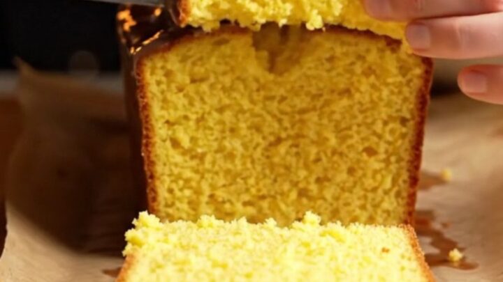Whole lemon cake with white glaze on a serving plate, sliced to show moist yellow crumb