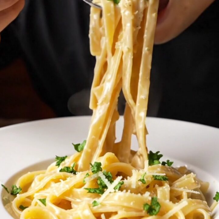 A fork twirling fettuccine Alfredo with creamy garlic parmesan sauce