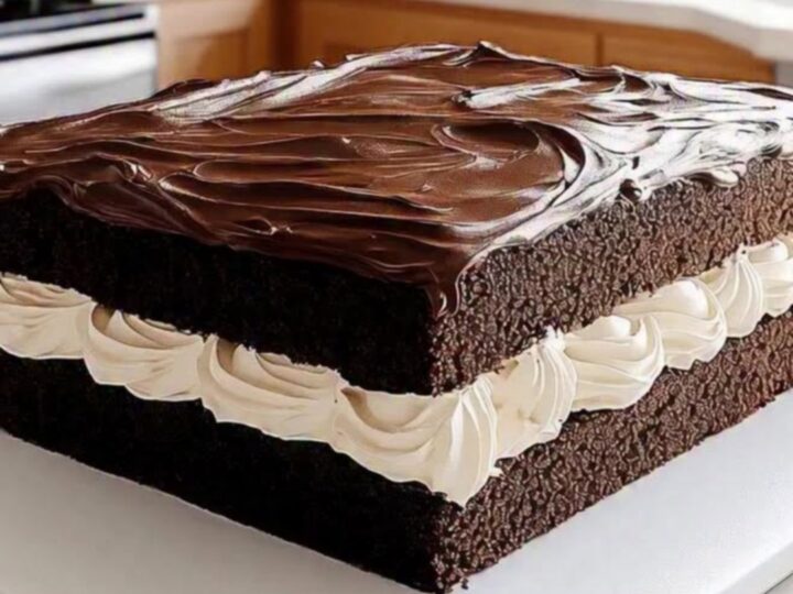 A top-down view of a square chocolate cake with a glossy ganache glaze on a white board.