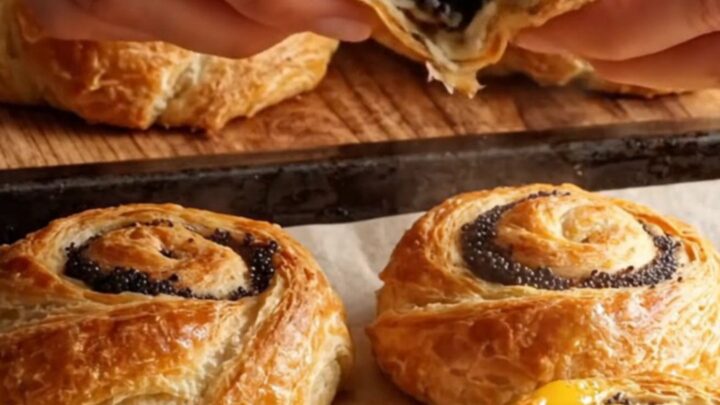 Golden flaky sweet poppy layer buns on a baking sheet, showing spiral layers and glossy top