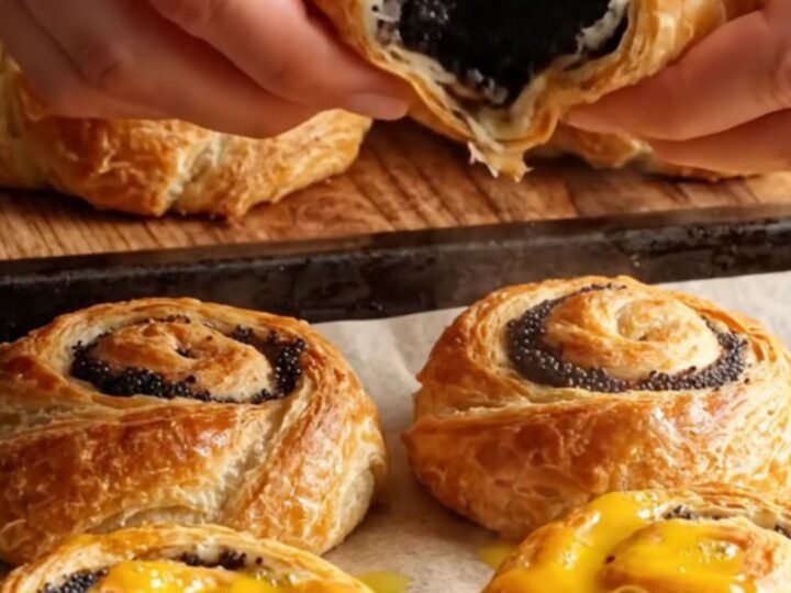 Golden flaky sweet poppy layer buns on a baking sheet, showing spiral layers and glossy top