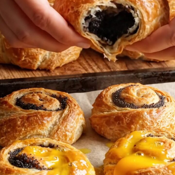 Golden flaky sweet poppy layer buns on a baking sheet, showing spiral layers and glossy top