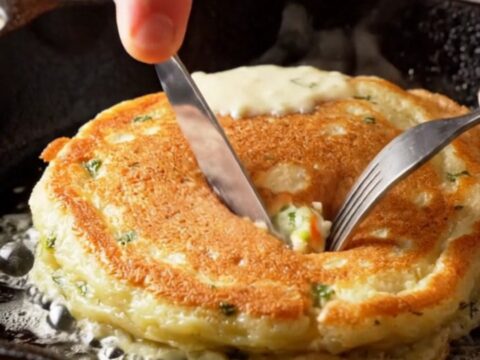 Stack of golden fluffy savory pancakes with dill and feta, broken open to show steamy cheese pockets