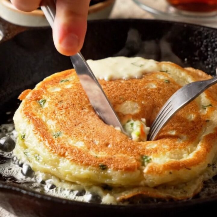 Stack of golden fluffy savory pancakes with dill and feta, broken open to show steamy cheese pockets