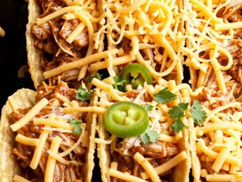 Crispy taco shells filled with shredded chicken and topped with melted cheese, garnished with sour cream, jalapeños