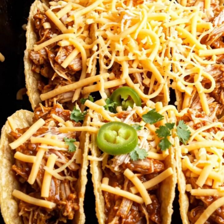 Crispy taco shells filled with shredded chicken and topped with melted cheese, garnished with sour cream, jalapeños