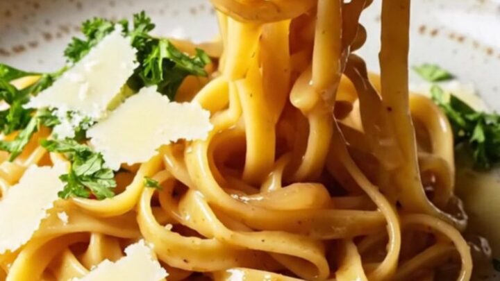 Twirled fettuccine in caramelized onion cream sauce on a rustic ceramic plate, topped with parsley and shaved Parmesan.