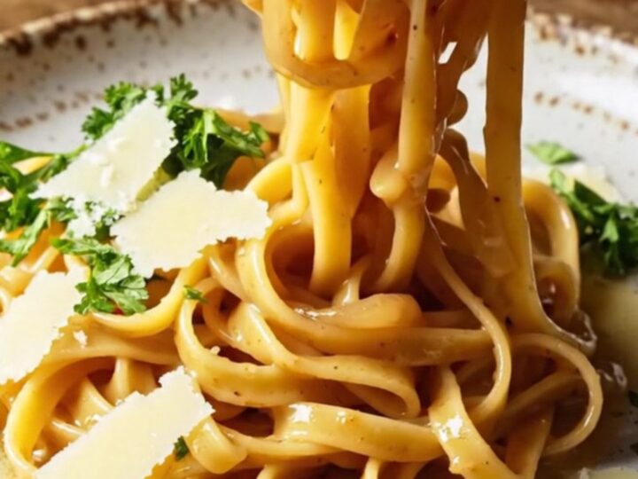 Twirled fettuccine in caramelized onion cream sauce on a rustic ceramic plate, topped with parsley and shaved Parmesan.