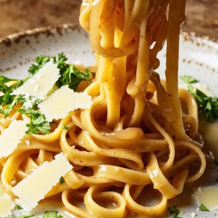 Twirled fettuccine in caramelized onion cream sauce on a rustic ceramic plate, topped with parsley and shaved Parmesan.