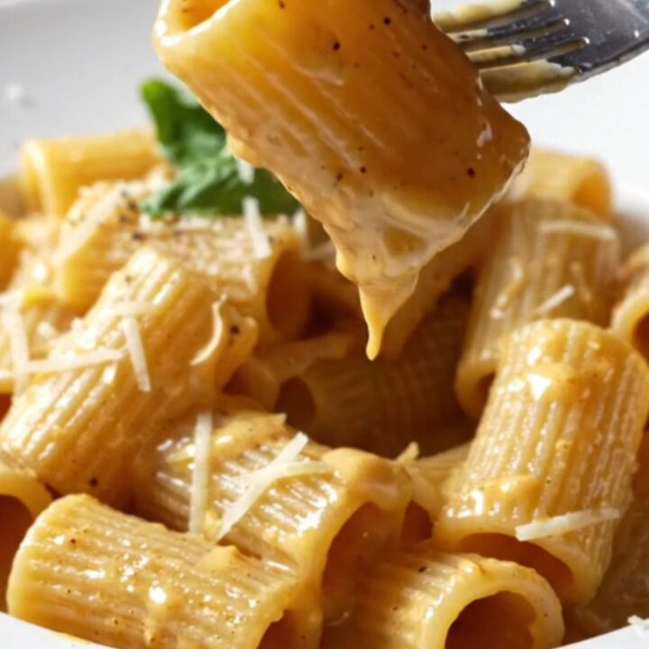 Creamy Tuscan Chicken Rigatoni in a skillet, garnished with fresh basil and cracked black pepper.