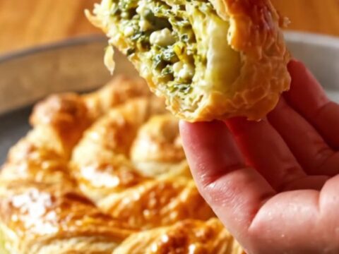 Golden twisted börek spiral on a baking sheet, sliced to show layers of flaky pastry and green filling