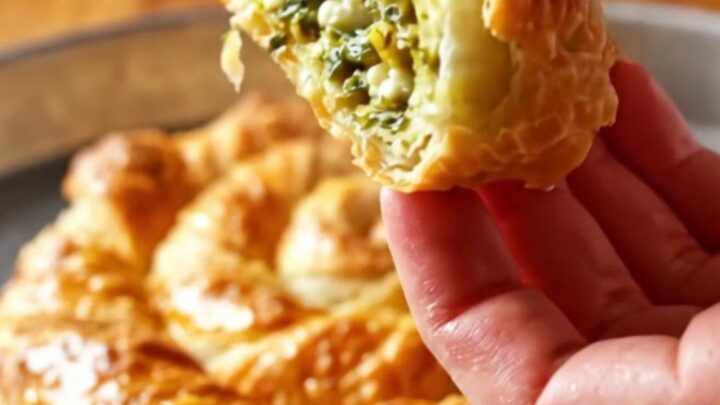 Golden twisted börek spiral on a baking sheet, sliced to show layers of flaky pastry and green filling