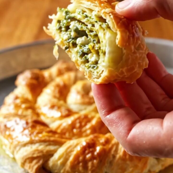 Golden twisted börek spiral on a baking sheet, sliced to show layers of flaky pastry and green filling