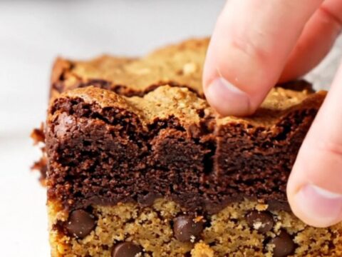 Thick brookie bars with a golden chocolate chip cookie base and a dark, fudgy brownie top, sliced and stacked.