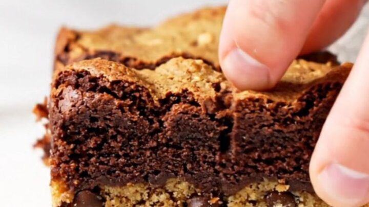 Thick brookie bars with a golden chocolate chip cookie base and a dark, fudgy brownie top, sliced and stacked.