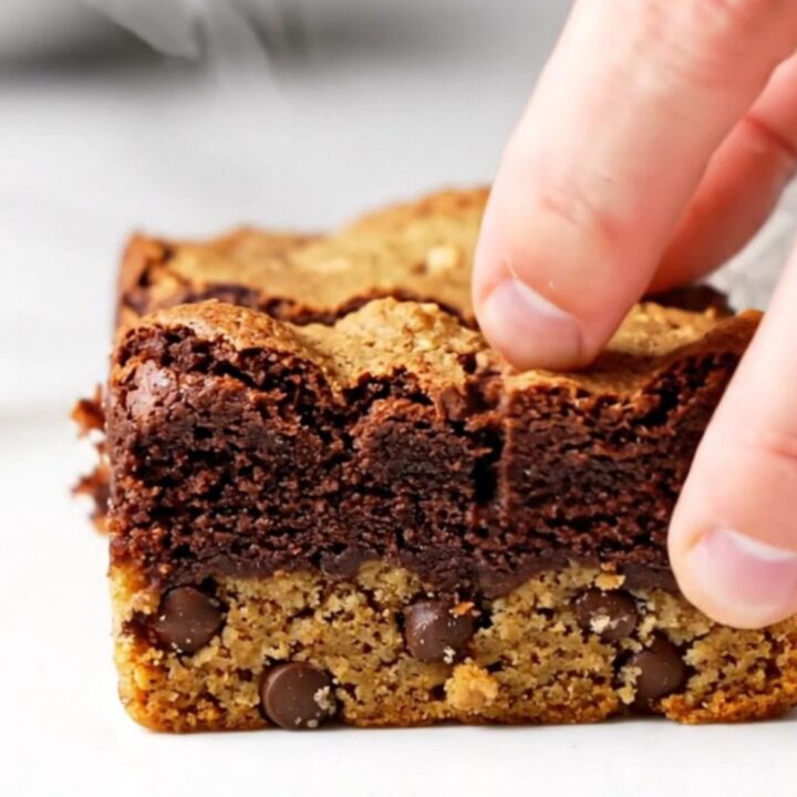 Thick brookie bars with a golden chocolate chip cookie base and a dark, fudgy brownie top, sliced and stacked.