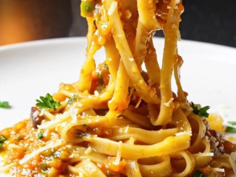 Golden tagliatelle twirled high on a plate, coated in a glossy vegetable sauce with fresh parsley and melted Parmesan.