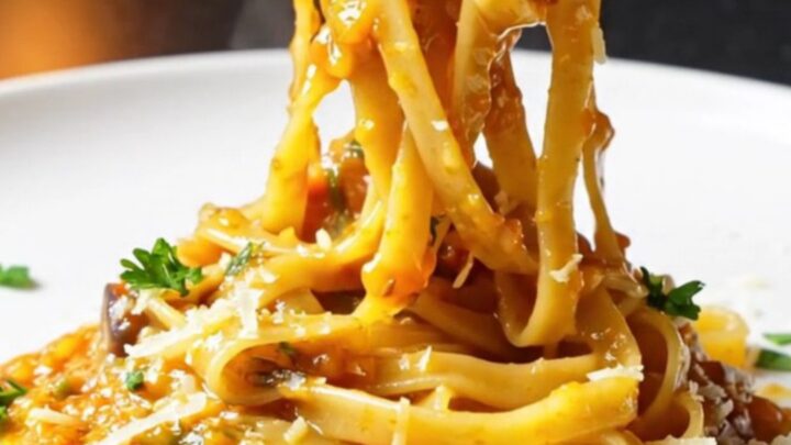 Golden tagliatelle twirled high on a plate, coated in a glossy vegetable sauce with fresh parsley and melted Parmesan.