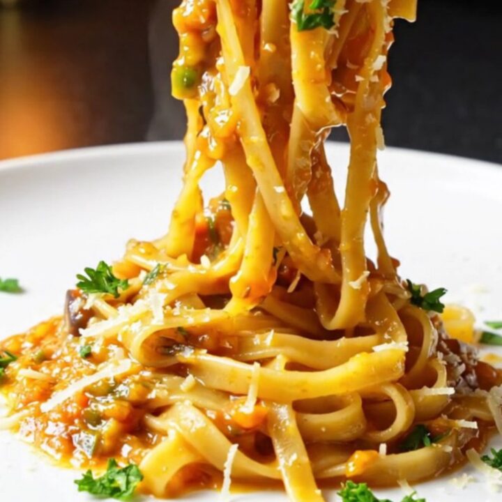 Golden tagliatelle twirled high on a plate, coated in a glossy vegetable sauce with fresh parsley and melted Parmesan.