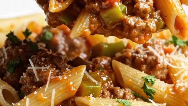 Steaming penne with meatball ragù in a deep pan, garnished with parsley and Parmesan.