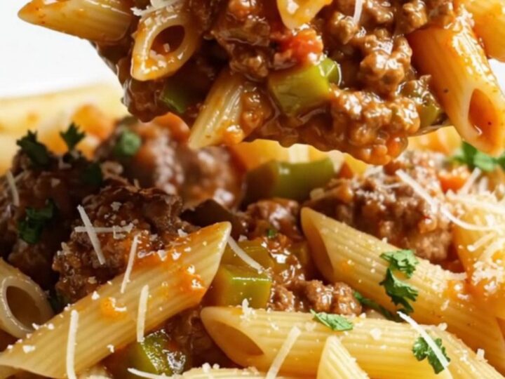 Steaming penne with meatball ragù in a deep pan, garnished with parsley and Parmesan.