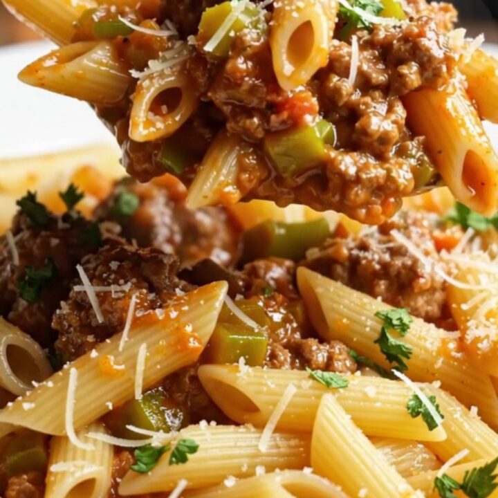 Steaming penne with meatball ragù in a deep pan, garnished with parsley and Parmesan.