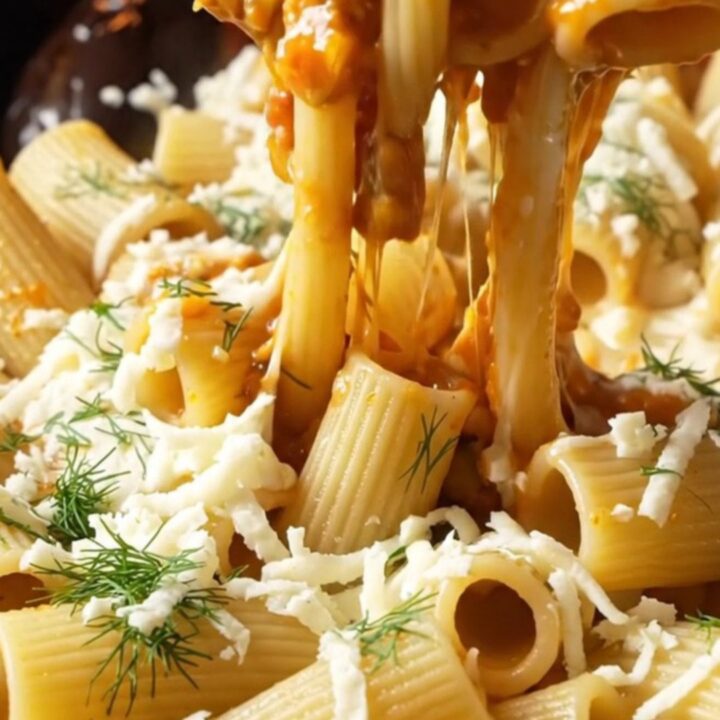 Spoon lifting cheesy pipe rigate pasta with long mozzarella strings and vegetable bits