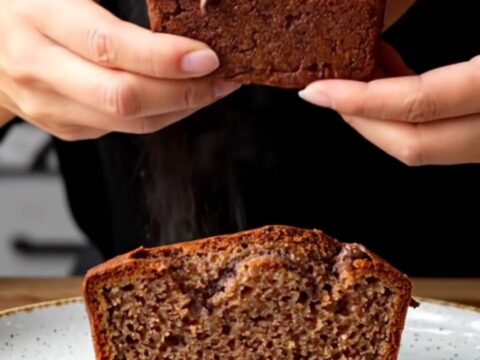 A slice of brown butter chocolate chip banana bread on a wooden board, showing moist crumb and melted chocolate