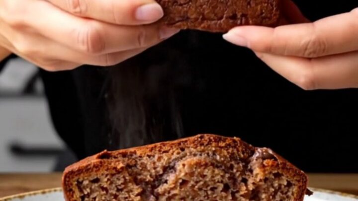 A slice of brown butter chocolate chip banana bread on a wooden board, showing moist crumb and melted chocolate
