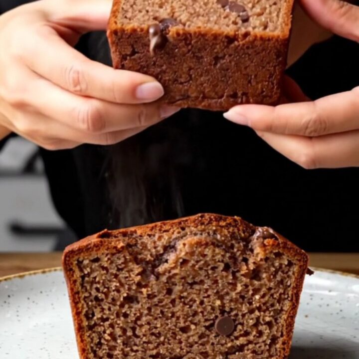 A slice of brown butter chocolate chip banana bread on a wooden board, showing moist crumb and melted chocolate
