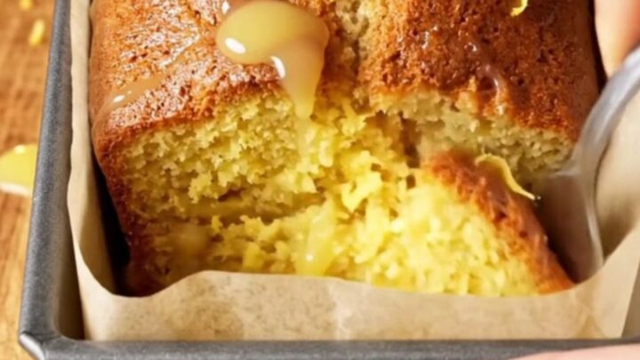 Whole lemon blender loaf cake with white glaze and lemon zest on top, sliced to show moist yellow crumb.