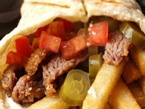 Crispy beef shawarma wraps sliced diagonally, showing juicy beef, fries, and garlic sauce inside golden pita