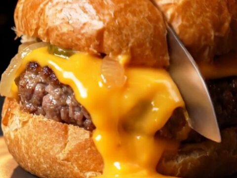 Golden brioche pockets with sesame seeds, one sliced open showing molten cheddar and juicy beef