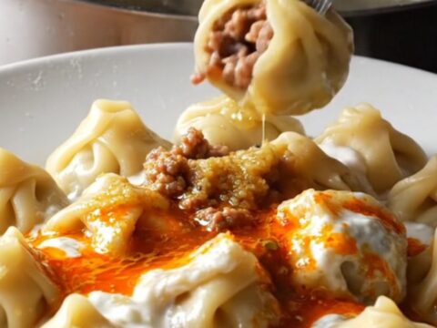 Honeycomb Turkish mantı dumplings in a shallow bowl, topped with garlic yogurt and sizzling red paprika mint butter.