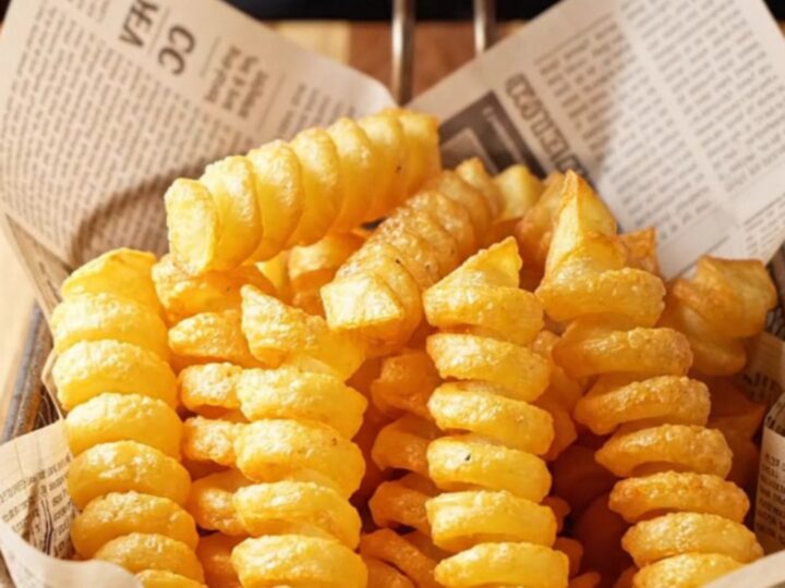 Golden spiral potato fries piled high on a paper-lined basket, with a crispy texture visible.