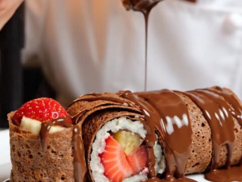 Chocolate crepe dessert sushi rolls sliced and arranged on a plate, showing strawberry and banana centers