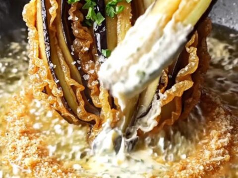 A golden-brown blooming eggplant fan on a rustic platter, garnished with parsley and sea salt