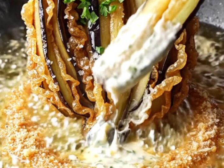 A golden-brown blooming eggplant fan on a rustic platter, garnished with parsley and sea salt