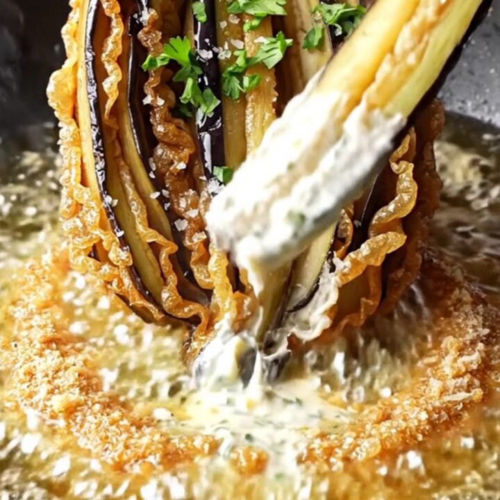 A golden-brown blooming eggplant fan on a rustic platter, garnished with parsley and sea salt