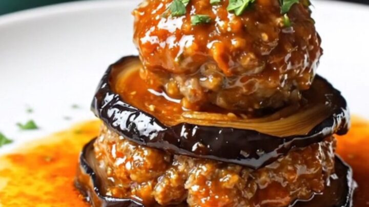Baked eggplant and meatball casserole with tomato glaze, bubbling and browned in a round dish.