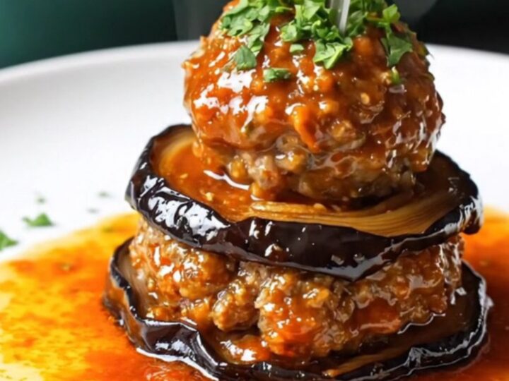 Baked eggplant and meatball casserole with tomato glaze, bubbling and browned in a round dish.
