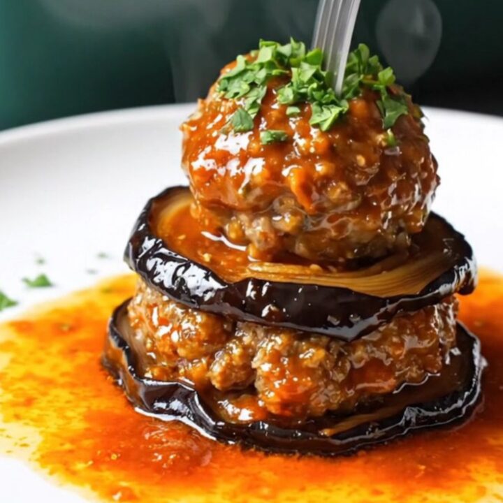 Baked eggplant and meatball casserole with tomato glaze, bubbling and browned in a round dish.