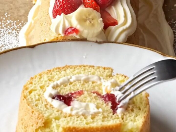 Swiss roll dusted with powdered sugar, topped with cream rosettes and berries, slice showing fruit filling